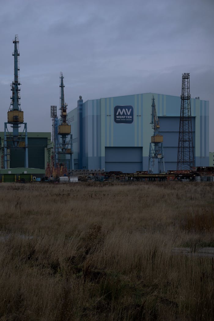 story-02 A large shipyard building with cranes at dusk, showcasing an industrial setting.