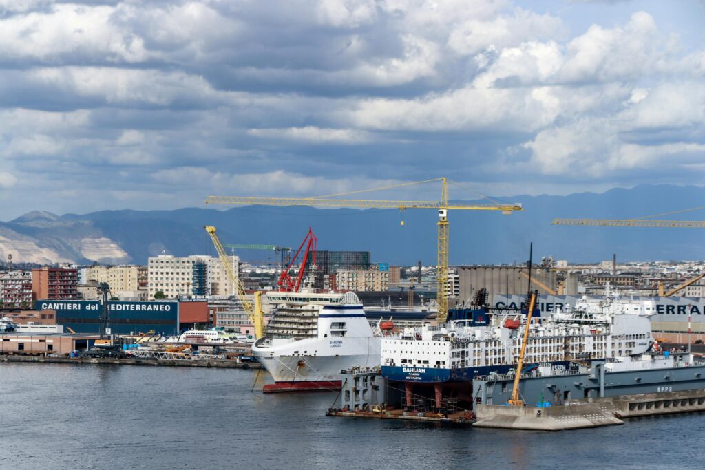pexels photo 34159693 34159693 A cruise ship docked at the bustling Port of Naples with cityscape and cranes in the background.