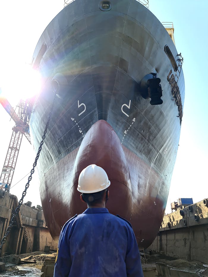 A worker examining a large ship in a Central Java dockyard under bright daylight.